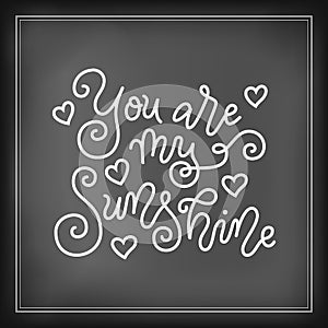 Modern mono line calligraphy lettering of You are my sunshine in white on chalkboard background with hearts