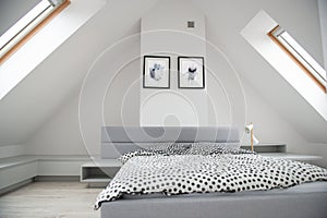 Modern monochrome design home interior of bedroom room in mansard with wooden bed and elegant accessories. Stylish home decor with