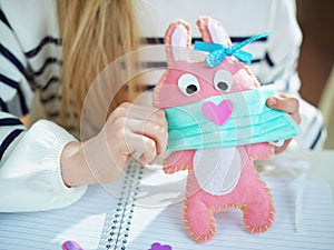 Modern mother and daughter wearing medical mask to toy rabbit