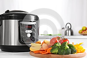 Modern multi cooker and wooden board with vegetables on white table