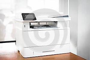 Modern multifunction printer with touchscreen interface placed on wooden desk in office. Suitable for business printing, scanning