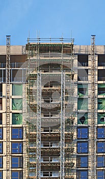 modern multistory apartment building under construction with scaffolding and hoist frames under a blue sky