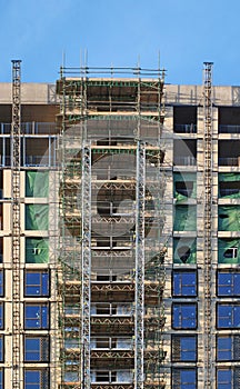modern multistory apartment building under construction with scaffolding and hoist frames under a blue sky