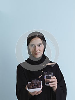 Modern muslim woman in abaya holding a date fruit and glass of water in front of her