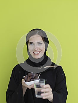 Modern muslim woman in abaya holding a date fruit and glass of water in front of her