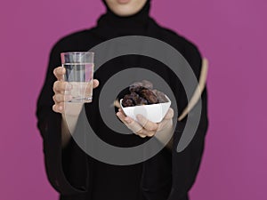 Modern muslim woman in abaya holding a date fruit and glass of water in front of her