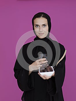 Modern muslim woman in abaya holding a date fruit and glass of water in front of her