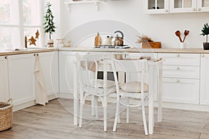 Modern new bright kitchen interior with white furniture and a dining table. gas stove with kettle and pan