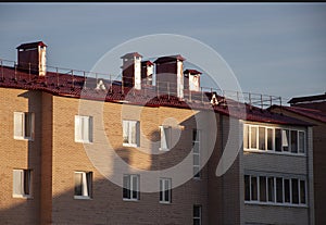 Modern new building with a lot of flats. There are windows and balconies. Light blue sky above