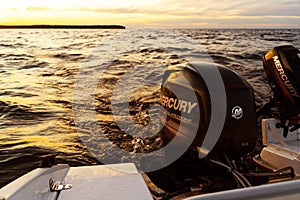 Modern new fishing sport boat with a brand new Mercury FourStroke outboard engine on the lake at the sunset or sunrise