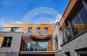 Modern new house exterior, facade with natural wood and many windows on blue sky background