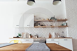 Modern new light interior of kitchen with white furniture and dining table.