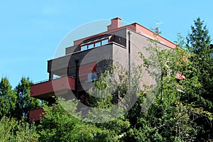 Modern newly built multi storey suburban house with large balconies surrounded with dense forest and clear blue sky