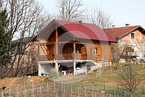 Modern newly built wooden log house with big open porch in front and new roof tiles on side of small hill