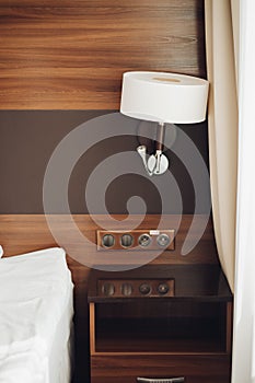 Modern night lamp and bedside table with sockets near bed surrounded by luxury hotel interior