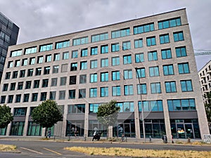 Modern office building with grey facade and many small windows reflecting the cloudy sky in the background