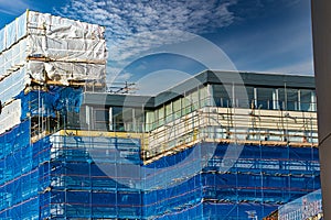 Modern office building under construction with scaffolding and blue safety netting against a cloudy sky in Harrogate, England