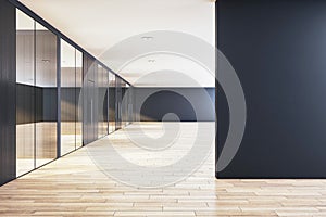 Modern office corridor with glass partitions, blank black wall space for mockups, herringbone wood floor, and ambient lighting,