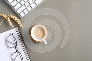 Modern office desk table with coffee cup, computer keyboard, paper notebook, glasses, wheat on green background. Flat lay, top