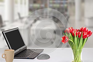 Modern office desk workplace with laptop computer with blank screen mockup on table a cup of coffee and a bouquet of tulips over