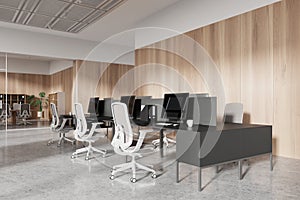 A modern office interior with desks, chairs, computers, and decorative plants against a wooden wall and glass partitions, concept photo