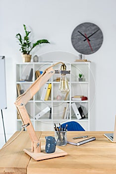 Modern office interior with wooden table, desklamp and stationery placed