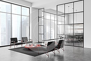 Modern office lounge with black chairs, a red table, and a large window overlooking a cityscape, with a spacious, light