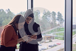 In a modern office a pair of colleagues, one wearing a hijab, engage in a lively discussion, sharing their business