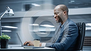 Modern Office: Successful Businessman Sitting at Desk Using Laptop Computer. African American Entr