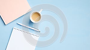 Modern office table with blank notepad, cup of coffee, pink paper notebook, pen on blue background. Minimal style feminine