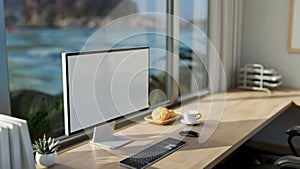 A modern office workspace with a computer mockup on a table against the window with a beach view