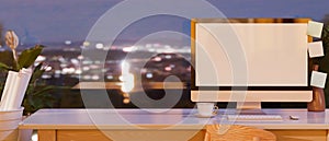 Office workspace with desktop computer mockup over evening view in the background