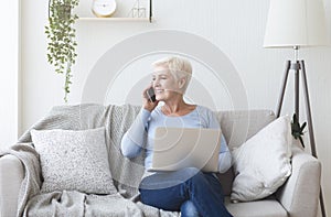 Modern old lady holding laptop and talking by phone