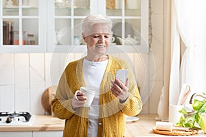 Modern old lady using mobile phone while drinking tea