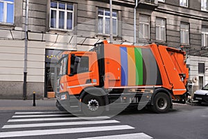 Modern orange garbage truck on city road outdoors