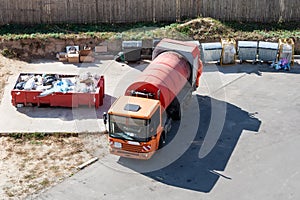 Modern orange gas-powered garbage truck with a cylinder tank for compacting garbage near plastic, metal and filled garbage