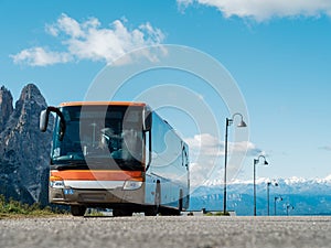 Modern orange tour bus parked in a tourist spot on a sunny day near rocky mountains. Tourism concept