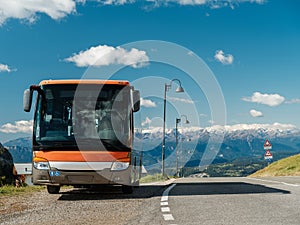 Modern orange tour bus parked in a tourist spot on a sunny day near rocky mountains. Tourism concept