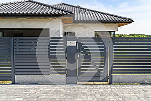 Modern panel fencing in anthacite color, visible wicket with videophone and a house in the background. photo