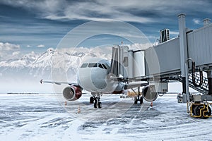 Modern passenger jetliner at the skybridge at winter airport apron on the background of high scenic mountains