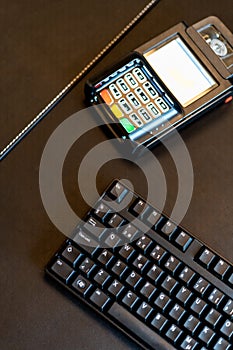 Modern payment terminal and credit cards on black background with computer keyboard, top view