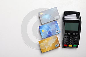 Modern payment terminal and credit cards on white table, flat lay. Space for text