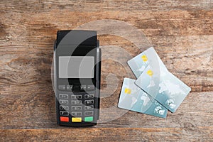 Modern payment terminal and credit cards on wooden background