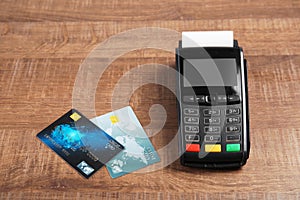 Modern payment terminal and credit cards on wooden background.