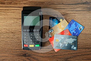 Modern payment terminal and credit cards on wooden table, flat lay