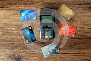 Modern payment terminal and credit cards on wooden table, flat lay