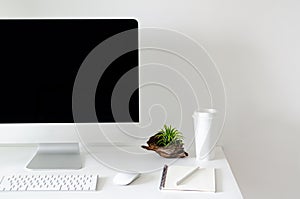 Modern personal computer screen on white table with a cup of coffee and Tillandsia air plant with space for text on white wall for