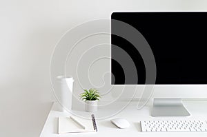 Modern personal computer screen on white table with a cup of coffee and Tillandsia air plant with space for text on white wall for