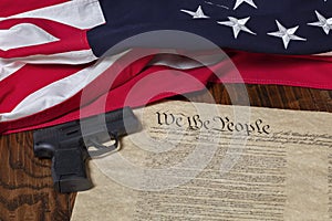 Modern pistol with thirteen star flag and the constitution of the United States on dark wood background