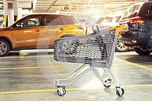 Modern plastic empty shopping cart left at roofed underground parking of shopping mall. Supermarket trolley with blurred parked